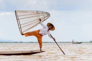 Inle Lake, Myanmar - 30 Ağustos 2016: Tanımlanamayan Birmanyalı balıkçı, özel el yapımı ağı olan bir teknede komik bir duruş sergiliyor. Bu Myanmar balıkçılık geleneksel yoludur
