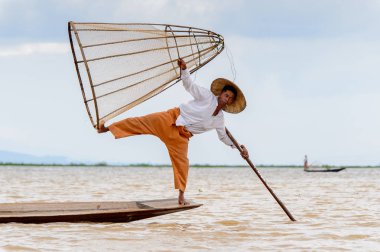 Inle Lake, Myanmar - 30 Ağustos 2016: Tanımlanamayan Birmanyalı balıkçı, özel el yapımı ağı olan bir teknede komik bir duruş sergiliyor. Bu Myanmar balıkçılık geleneksel yoludur