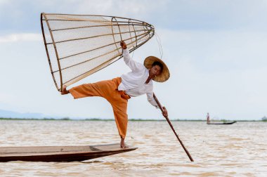 Inle Lake, Myanmar - 30 Ağustos 2016: Tanımlanamayan Birmanyalı balıkçı, özel el yapımı ağı olan bir teknede komik bir duruş sergiliyor. Bu Myanmar balıkçılık geleneksel yoludur