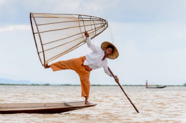 Inle Lake, Myanmar - 30 Ağustos 2016: Tanımlanamayan Birmanyalı balıkçı, özel el yapımı ağı olan bir teknede komik bir duruş sergiliyor. Bu Myanmar balıkçılık geleneksel yoludur