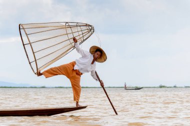 Inle Lake, Myanmar - 30 Ağustos 2016: Tanımlanamayan Birmanyalı balıkçı, özel el yapımı ağı olan bir teknede komik bir duruş sergiliyor. Bu Myanmar balıkçılık geleneksel yoludur