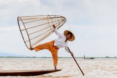 Inle Lake, Myanmar - 30 Ağustos 2016: Tanımlanamayan Birmanyalı balıkçı, özel el yapımı ağı olan bir teknede komik bir duruş sergiliyor. Bu Myanmar balıkçılık geleneksel yoludur