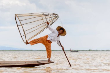 Inle Lake, Myanmar - 30 Ağustos 2016: Tanımlanamayan Birmanyalı balıkçı, özel el yapımı ağı olan bir teknede komik bir duruş sergiliyor. Bu Myanmar balıkçılık geleneksel yoludur