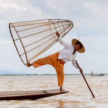 Inle Lake, Myanmar - 30 Ağustos 2016: Tanımlanamayan Birmanyalı balıkçı, özel el yapımı ağı olan bir teknede komik bir duruş sergiliyor. Bu Myanmar balıkçılık geleneksel yoludur