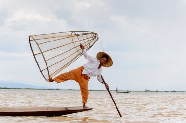 Inle Lake, Myanmar - 30 Ağustos 2016: Tanımlanamayan Birmanyalı balıkçı, özel el yapımı ağı olan bir teknede komik bir duruş sergiliyor. Bu Myanmar balıkçılık geleneksel yoludur