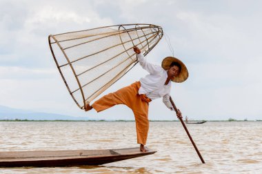 Inle Lake, Myanmar - 30 Ağustos 2016: Tanımlanamayan Birmanyalı balıkçı, özel el yapımı ağı olan bir teknede komik bir duruş sergiliyor. Bu Myanmar balıkçılık geleneksel yoludur