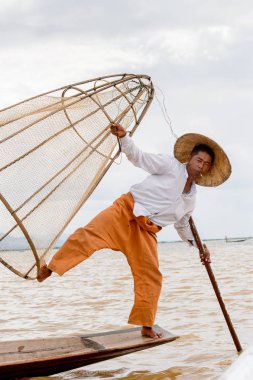Inle Lake, Myanmar - 30 Ağustos 2016: Tanımlanamayan Birmanyalı balıkçı, özel el yapımı ağı olan bir teknede komik bir duruş sergiliyor. Bu Myanmar balıkçılık geleneksel yoludur