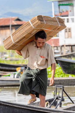 Inle Lake, Myanmar - 30 Ağustos 2016: Kimliği belirsiz Birmanyalı adam, Shan Eyaleti'nin Taunggyi İlçesi'nin Nyaungshwe İlçesi'ndeki tatlı su gölü Inle Sap'ın üzerinde bambu teknesinde eşya taşıyor.