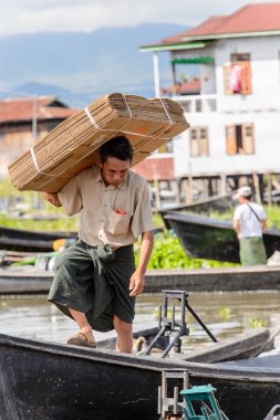 Inle Lake, Myanmar - 30 Ağustos 2016: Kimliği belirsiz Birmanyalı adam, Shan Eyaleti'nin Taunggyi İlçesi'nin Nyaungshwe İlçesi'ndeki tatlı su gölü Inle Sap'ın üzerinde bambu teknesinde eşya taşıyor.