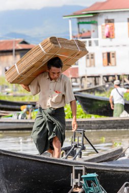 Inle Lake, Myanmar - 30 Ağustos 2016: Kimliği belirsiz Birmanyalı adam, Shan Eyaleti'nin Taunggyi İlçesi'nin Nyaungshwe İlçesi'ndeki tatlı su gölü Inle Sap'ın üzerinde bambu teknesinde eşya taşıyor.