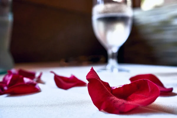 Red petals displayed on a white linen table with a glass filled with water in the back at a restaurant in Hawaii.