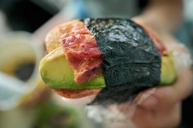 A close-up of musubi, a Japanese snack famous in Hawaii, composed of bacon, avocado, spam, and egg. clipart