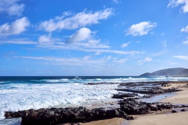 Güçlü dalgalar, güzel bulutlar ve sahilde dağılmış kayalar ile Hawaii Okyanusu görünümü.