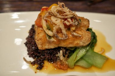 Bir tabak balık pirzola kalamar mürekkep risotto ve üstünde kızarmış kalamar yerde servis.