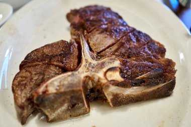 Bir restoranda beyaz tabakta servis edilen sulu t-kemikli biftek.