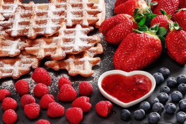 Kalp şeklinde bir daire içinde çilek reçeli döktü. Uçan daire yanındaki yaban mersini, ahududu ve çilek vardır. Ayrıca yanında gofret ile pudra şekeri serpilir.