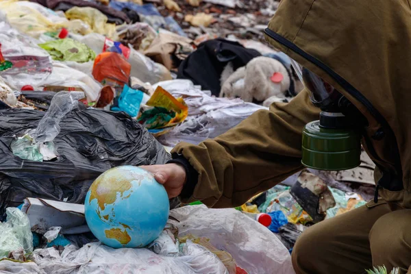 A man in a gas mask found a globe in the garbage. People are destroying planet earth. The world is caught up in plastic debris. The concept of hope to save a dying world