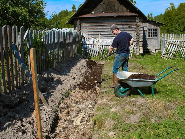 ラズベリーを植えるためのベッドの準備 堆肥は肥料としてもたらされます 男はトレンチに手押し車からシャベル堆肥を運ぶ — ストック写真