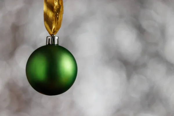 Green Christmas ball on a white bokeh background similar to snowflakes. There is space for copy space next to the Christmas ball.