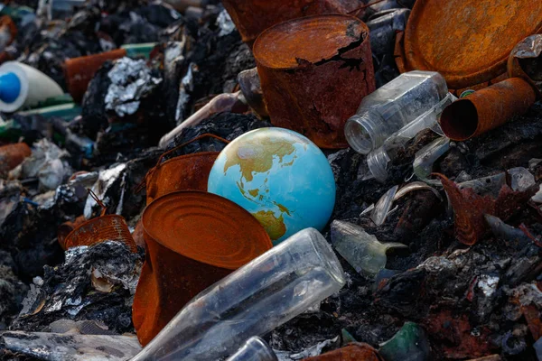 Planet earth thrown into a garbage dump. Burned garbage is lying around the ground: rusty iron cans, broken glass bottles. Environment day concept. Save the world from pollution by waste.