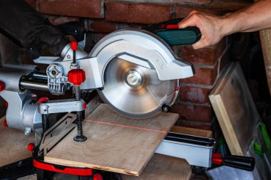 Works miter saw. The red line of the laser target pointer in the place of the future cut. The hand of a carpenter man controls the saw. clipart