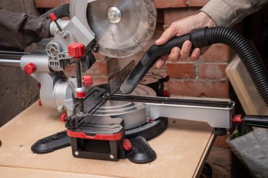 Bir marangoz atölyesinde çöp toplama. Erkek el elektrikli süpürge hortumu tutuyor. Talaş ve cips, gönye testerinden çıkarılır.