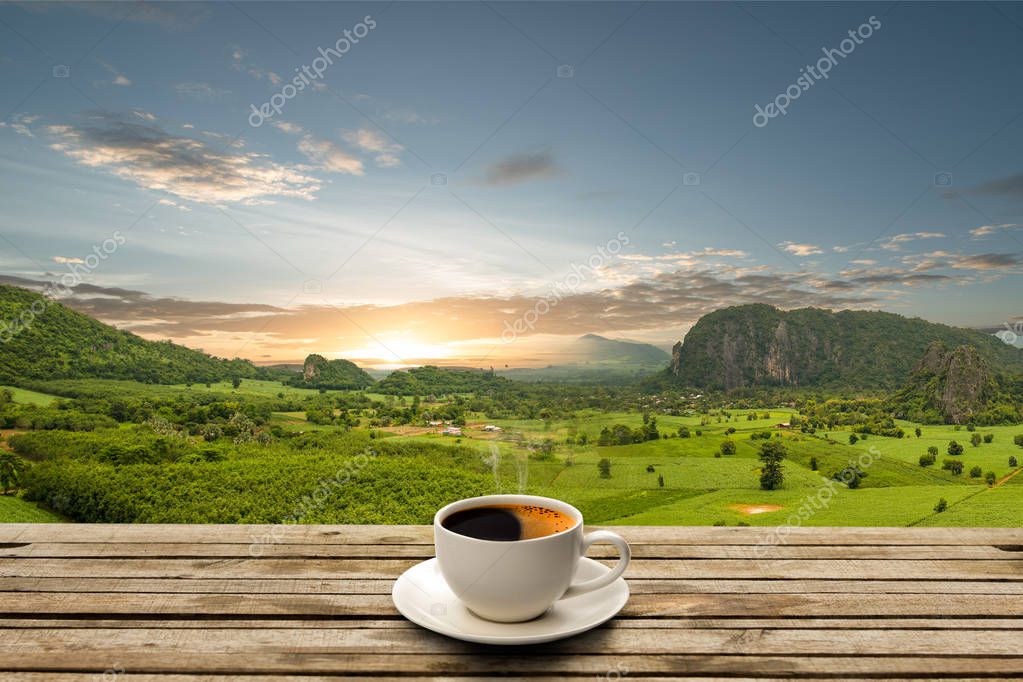Coffee cup on wooden table with blue sky and beautiful mountain with sunrise