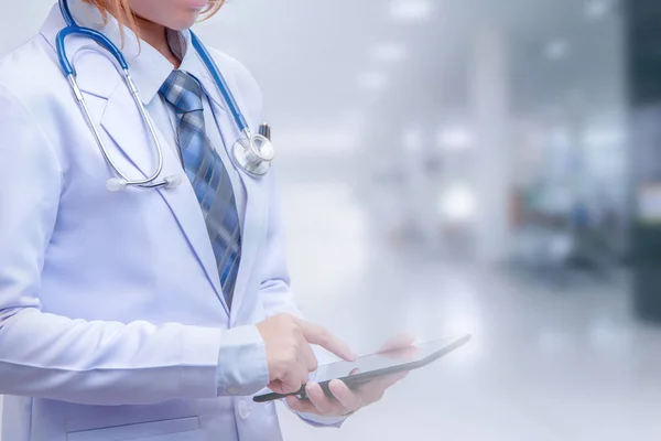 smart woman doctor holding tablet and pointing to screen on blurry out patient department of hospital, conception of modern medical with technology and data conection for early diagnosis