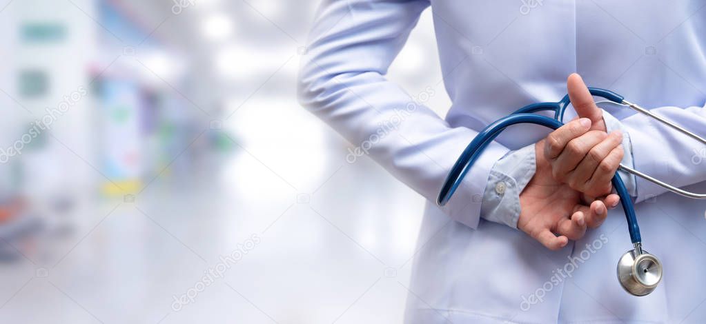 woman doctor crossed arm and holding stethoscope behind back on blurred out patient department, medical concept 
