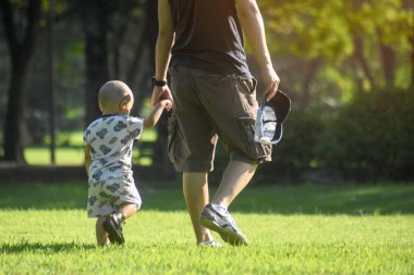 Baba ve oğul parkta, çim zemin yürürken elini tut