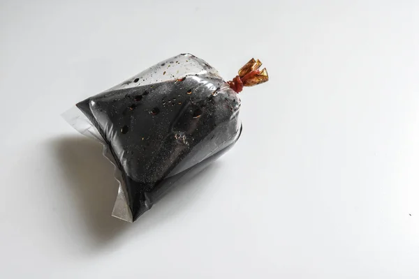 sıkıca kauçuk ile dolu bir plastik torba içinde soya sosu daldırma, beyaz arka planda siyah sos.