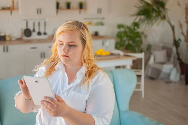 Young beautiful overweight woman makes online order in living room at home — Stock Photo, Image