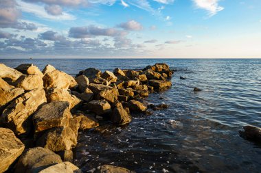 Taşlı deniz manzarası. Arka planda bulutlu mavi gökyüzü.