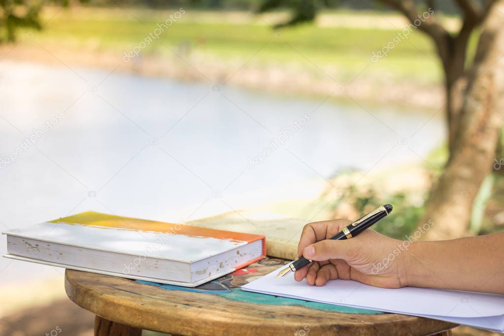 Man's hand with pen writing on notebook in park