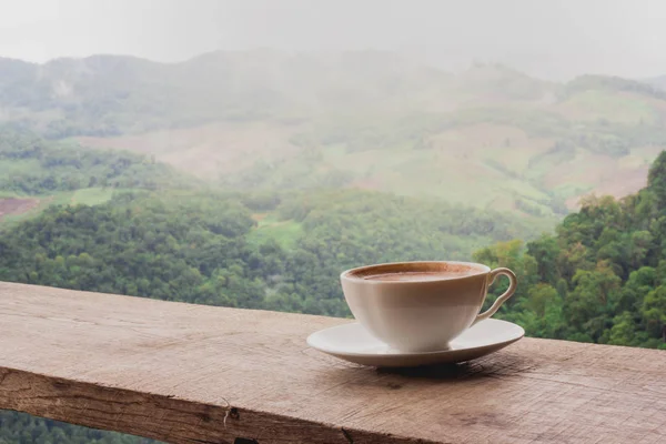 A cup of coffee on the table and a beautiful mountain background.