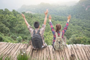 Sırt çantalı yürüyüşçüler bir dağın tepesinde dinleniyorlar ve vadinin manzarasının tadını çıkarıyorlar.
