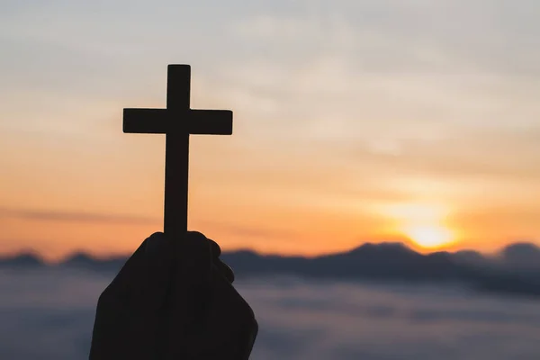 Silhouette off hands holding wooden cross  on sunrise background, Crucifix, Symbol of Faith.