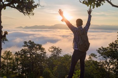 Turist ile dağ yamacında sırt çantası ile üzerine ellerini kaldırdı, vadi sis ile kaplıdır ve güzel gün doğumu vardır. Güzellik, Doğa, turizm ve seyahat kavramı.