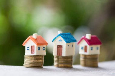 Arka plan olarak hesap makinesi ile sikke yığınları üzerinde Ev modeli. Emlak merdiveni, ipotek ve gayrimenkul yatırımı konsepti.