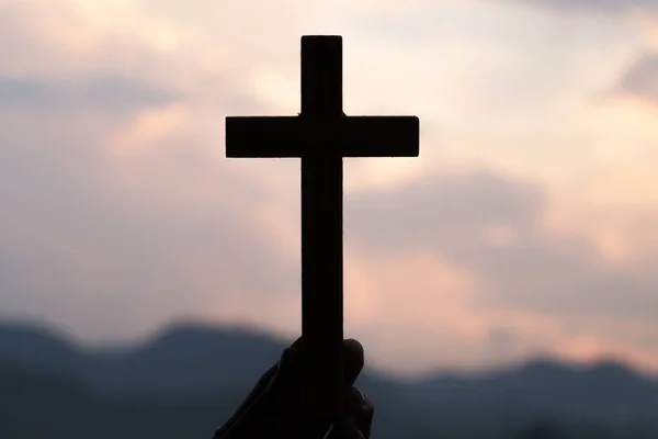 举行基督徒十字架圣洁推力的妇女手与轻的日落背景 — 图库照片