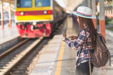 Güzel genç Asyalı kadın gezgin kahverengi çanta ile saat seyir tren tren istasyonunda bekleyen, Çinli turist, seyahat ve tatil kavramı.