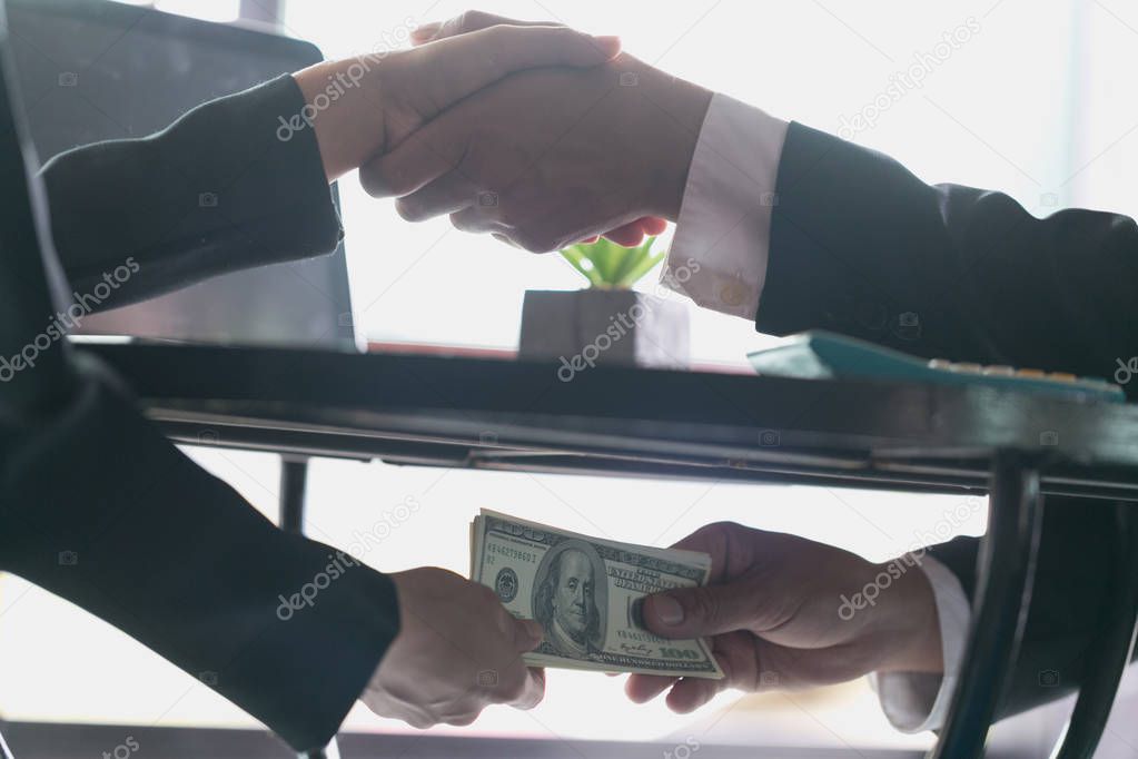 Corrupted businessman sealing the deal with a handshake and receiving a bribe money, anti bribery and corruption concepts