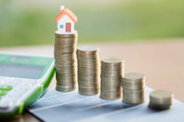Arka plan olarak hesap makinesi ile sikke yığınları üzerinde Ev modeli. Emlak merdiveni, ipotek ve gayrimenkul yatırımı konsepti.