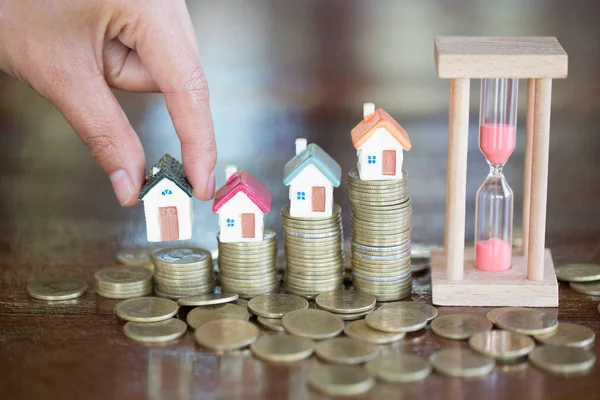 Woman hand hold a  home model put on the stack coin with growing in the public park, Savings money for buy house and loan to business investment for real estate concept.