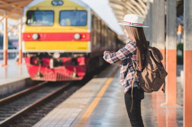 Güzel genç Asyalı kadın gezgin kahverengi çanta ile saat seyir tren tren istasyonunda bekleyen, Çinli turist, seyahat ve tatil kavramı.