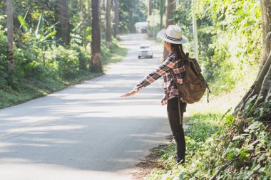 Sırt çantaları ile kadın turist ağaçları ve güzel doğa ile kırsal otobüs bekliyor.