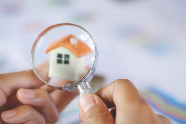 Yakın çekim A işadamı'nın el arıyorum, ev modeli aracılığıyla Büyüteç, ev arama kavramı bir büyüteç ile
