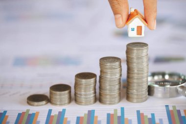 İnsan eli bozuk para yığınına ev modeli koyuyor. Emlak merdiveni, konut ve konut, ipotek ve emlak yatırımı kavramı.