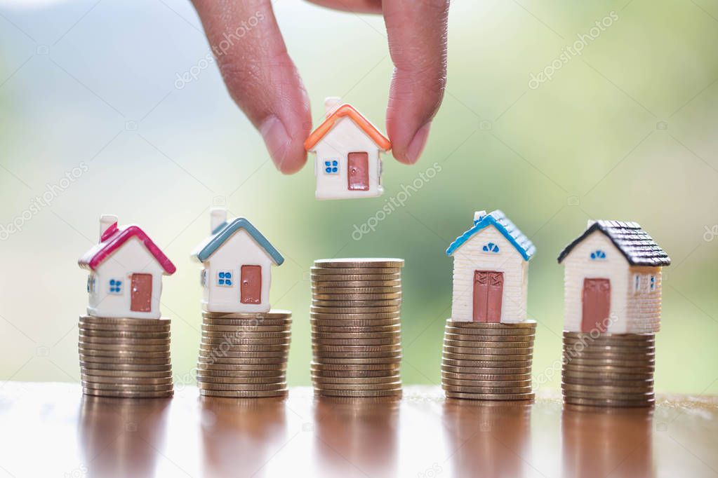 Human hand putting house model on coins stack,  planning savings money of coins to buy a home concept, mortgage and real estate investment.  saving or investment for a house.