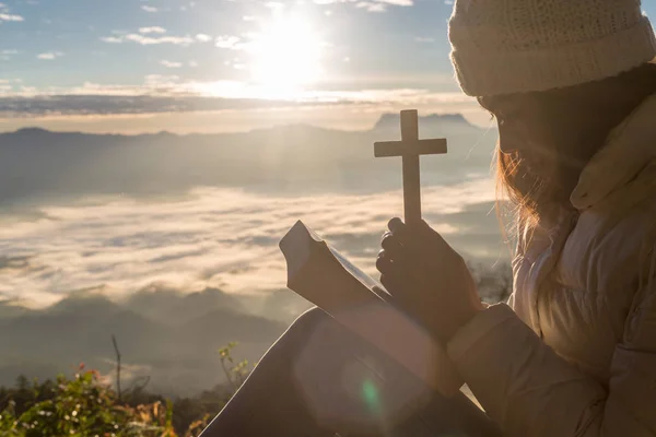 Women pray to god with the cross on the mountain background with morning sunrise. Woman Pray for god blessing to wishing have a better life. Christian life crisis prayer to god.